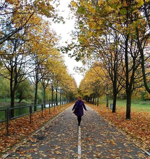Слънчева алея в парк с хора, които се разхождат спокойно сред зелени дървета